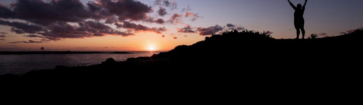 Silhouette of a person celebrating at a stunning sunset by the ocean.