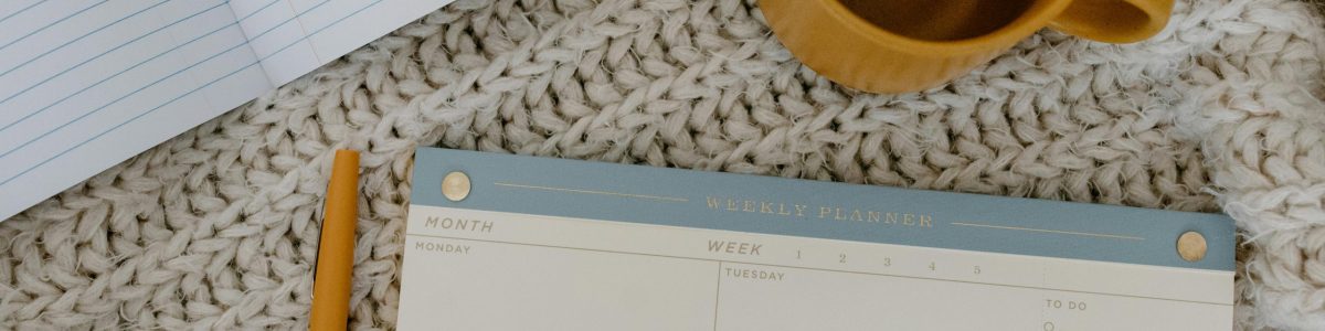 Flat lay of a planner, notebook, and coffee mug on a knitted blanket for a cozy planning session.